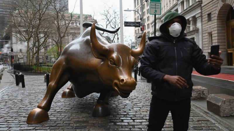 Man takes selfie near charging bull statue near NYSE in March 2020