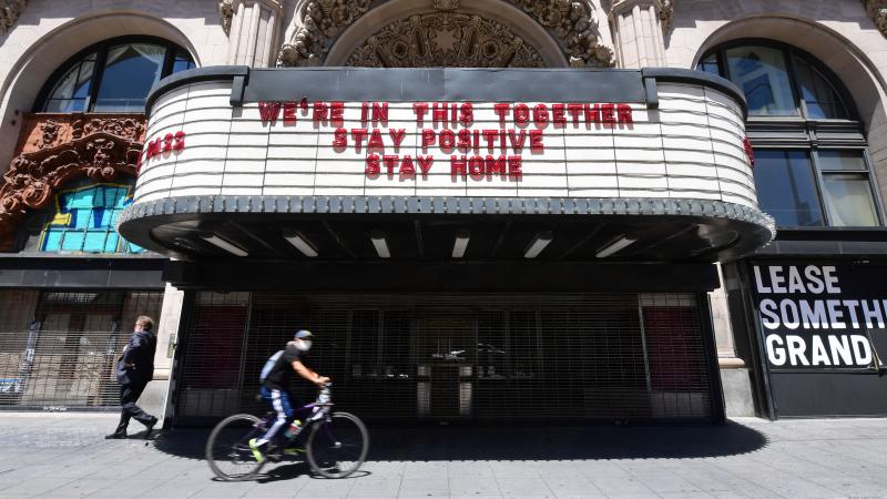 A cyclist in facemask rides past the Million Dollar Theater in LA, closed due to the coronavirus pandemic.