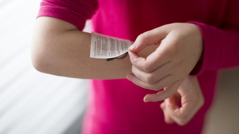 Child applying temporary tattoo to arm, cropped - stock photo
