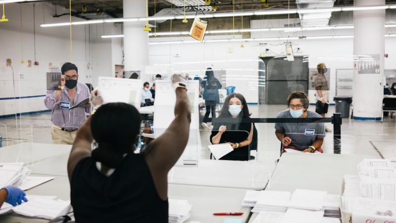 Campaign volunteers watch as an NYC Board of Elections official (second from left) presents an opened mail-in-ballot for review at a canvassing site in Manhattan in New York City