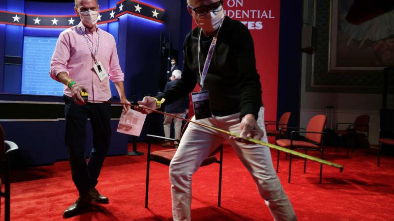 Staff members of the Commission on the Presidential Debates measure the distance between chairs for the audience in the debate hall ahead of the vice presidential debate