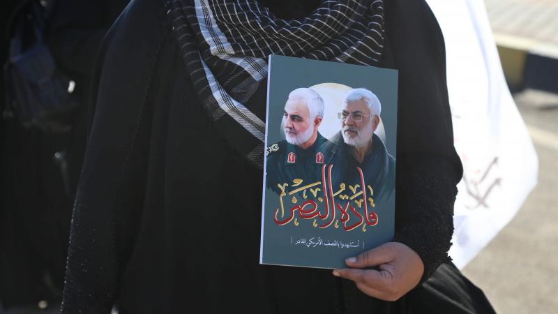 A mourner holds a portrait of Qasem Soleimani and Abu Mahdi al-Muhandis