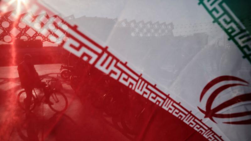 Iranian man with bicycle behind Iranian flag in February 2021