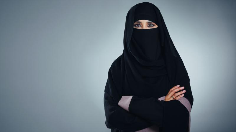 A woman in a Burqa stands with arms crossed
