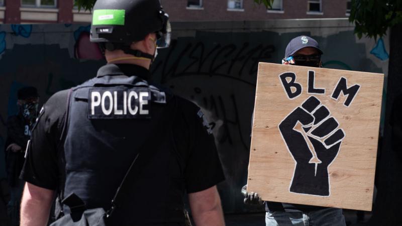 A police officer stands in front of a Black Lives Matter sign.