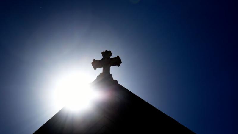The sun behind a stone cross on the Cathedral Basilica of St. Frances of Assisi in New Mexico in 2020