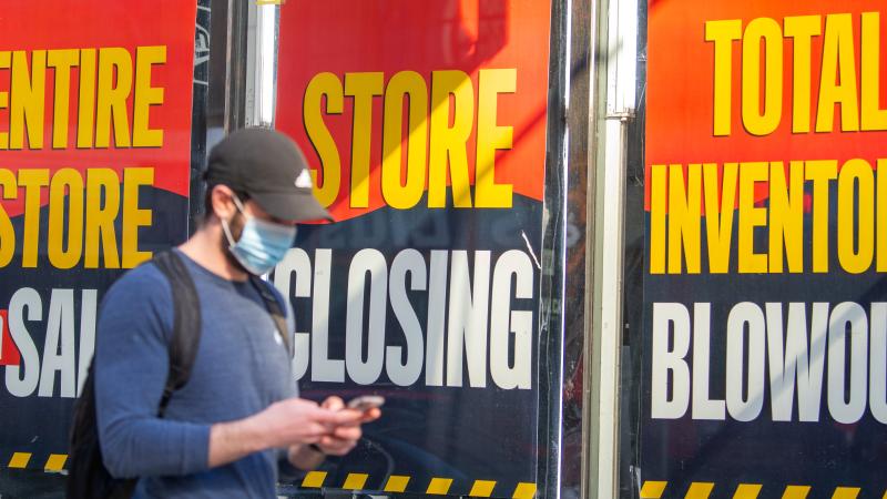 Man wearing mask walks past 'Store Closing' signs amid COVID-19 pandemic