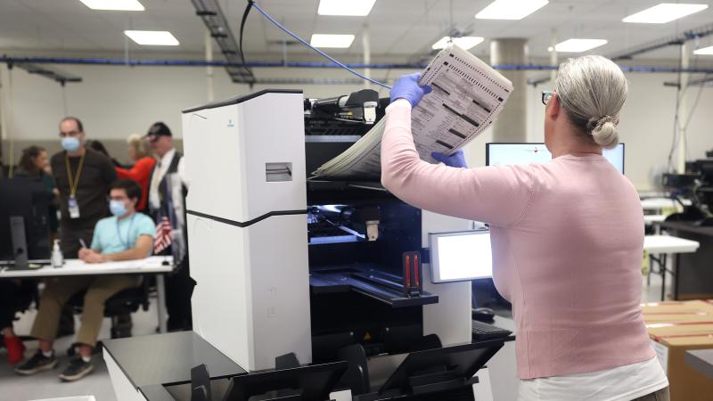 An election worker inserts a stack of ballots into a scanning machine at the Maricopa County Tabulation and Election Center on November 10, 2022 in Phoenix, Arizona.