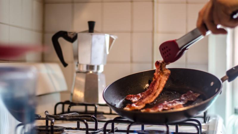 Cropped Hand Cooking Bacon On Stove In Kitchen 