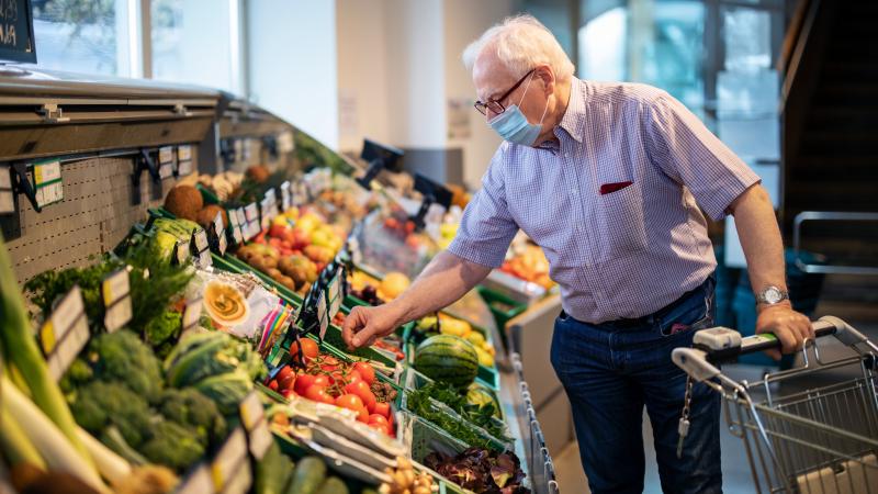 Senior man with face mask buying vegetables in grocery store (Germany)