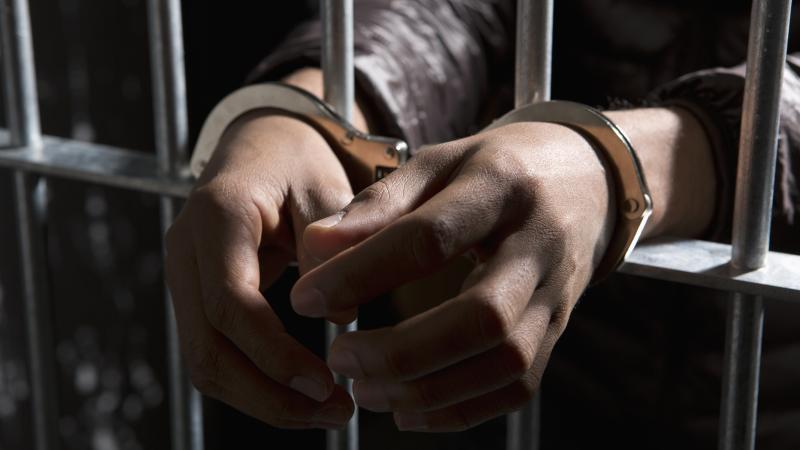 A prisoner behind bars with hands cuffed