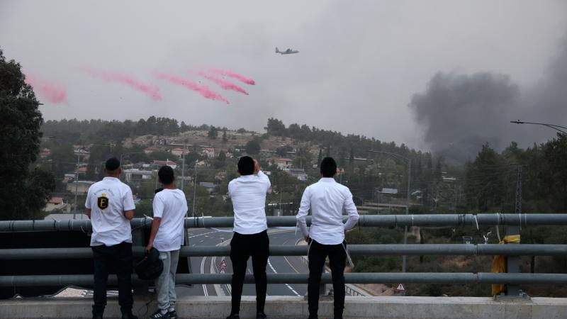 People watch as an army airplane drops fire retardant in the distance on April 30, 2025 in Jerusalem. Wildfires are spreading through the Jerusalem Hills, and high winds have caused many Independence Day events to be abandoned.