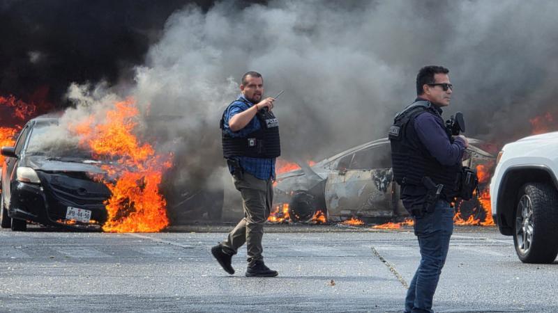 Police officers secure the area where vehicles were set on fire by organized crime members to block a road following a military operation