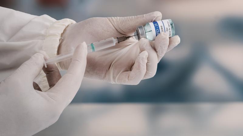 A young doctor in white protective glove is holding a medical syringe and vial